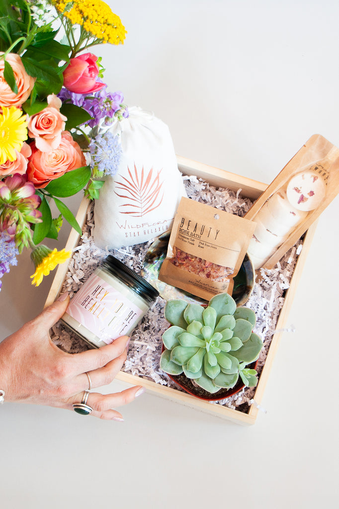 Gift box with flowers, candle, bath salts, lavender sachet, and a succulent on a white surface