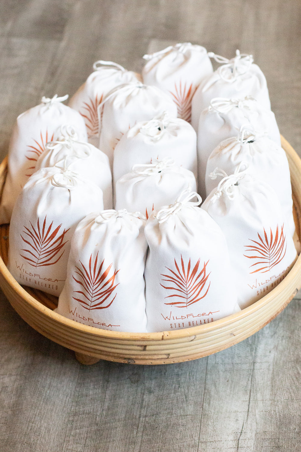 A bunch of white drawstring lavender-filled sachets with WildFlora palm leaf logo in a wood tray.