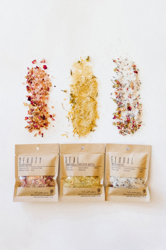 Three packages of WildFlora bath salts, spilled out on a white background