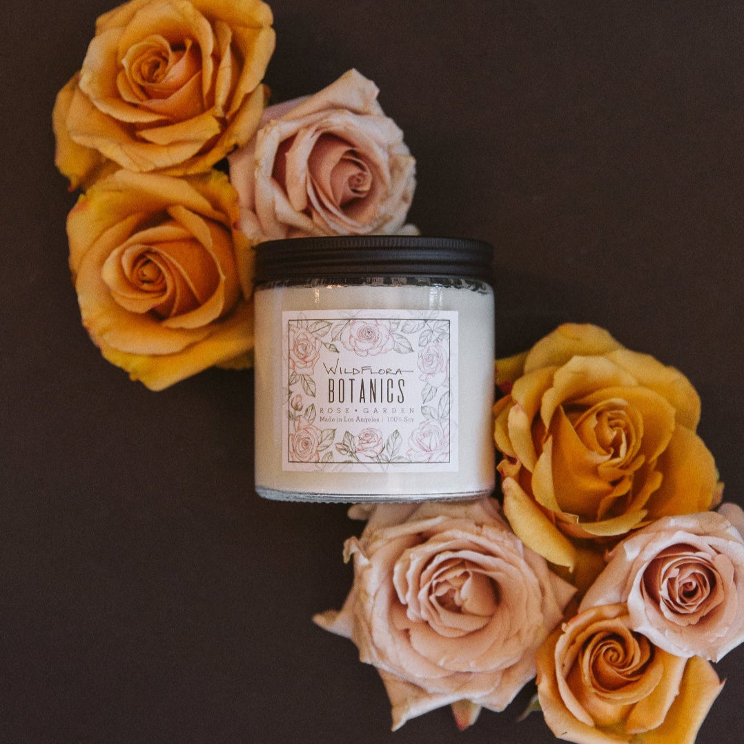 WildFlora Botanics Rose Garden Candle surrounded by yellow and pink roses on a dark background