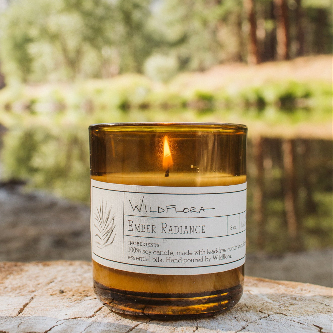 Candle labeled 'WildFlora Ember Radiance' on a log with a forest background