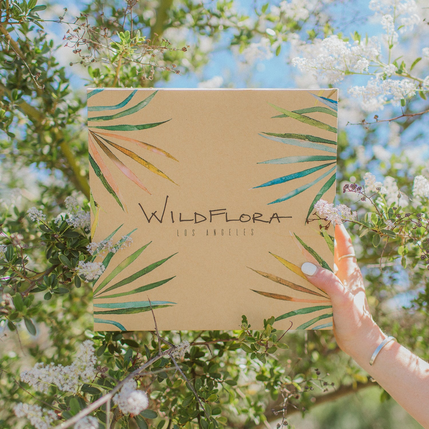 WildFlora shippable box, held in front of blooming shrub