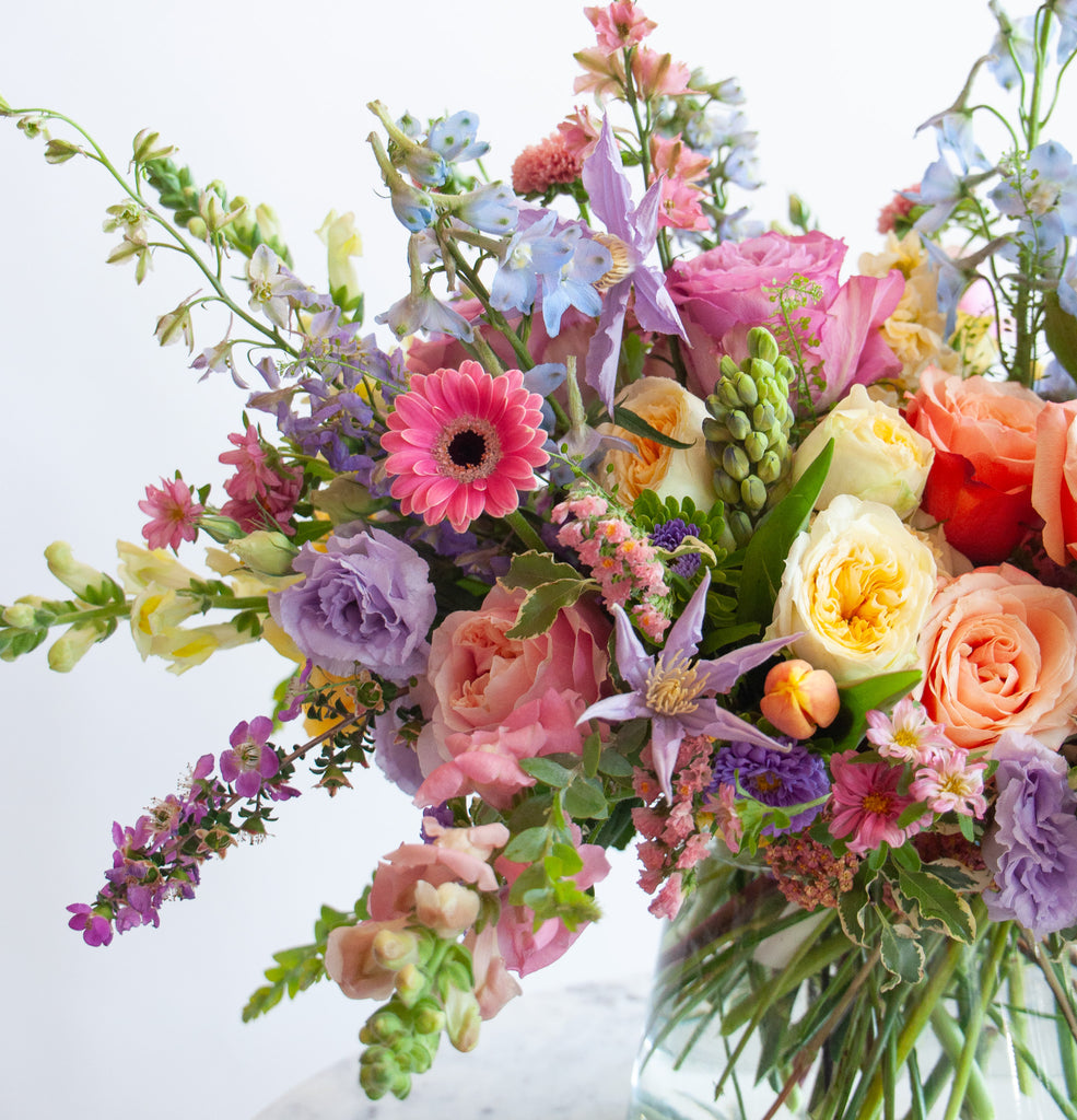 Close up of the blooms in a flower arrangement. The flowers are many colors and include roses, tulips, daisies, snapdragon, clematis, stock, hyacinth, and delphinium.