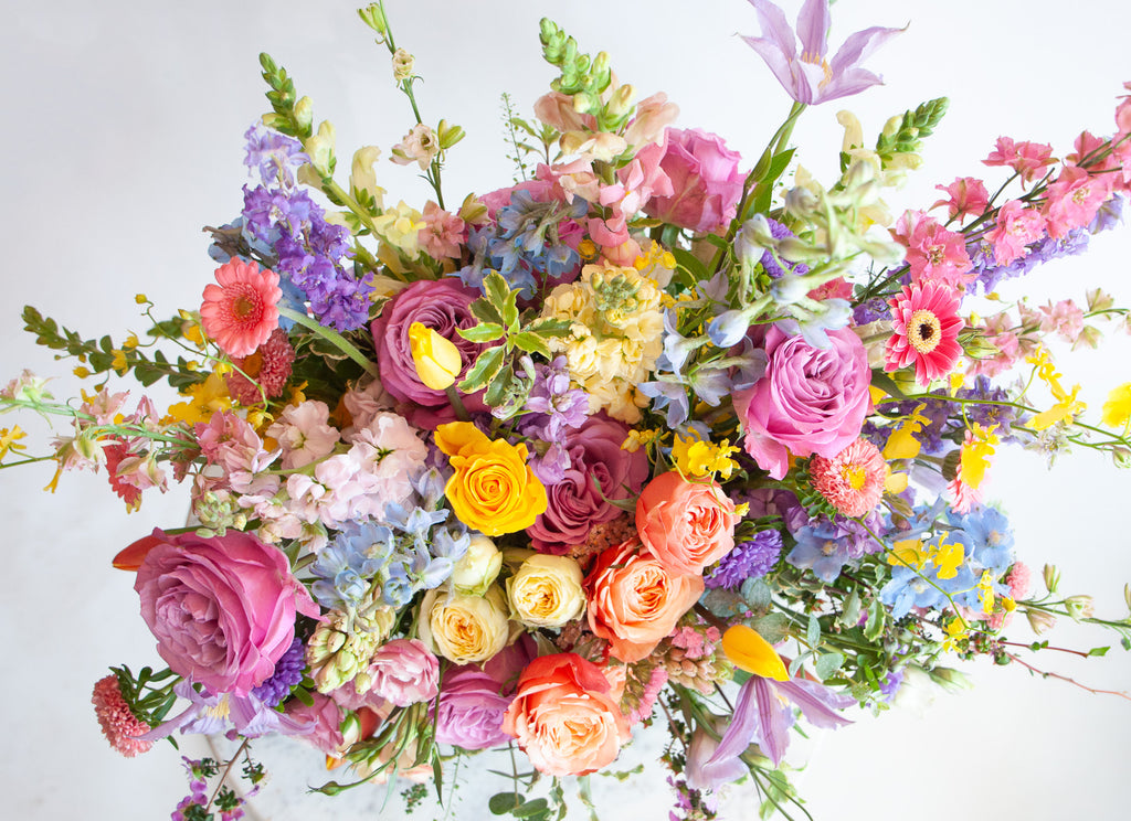 Close up of the blooms in a flower arrangement. The flowers are many colors and include roses, tulips, daisies, snapdragon, clematis, stock, hyacinth, orchids, and delphinium.