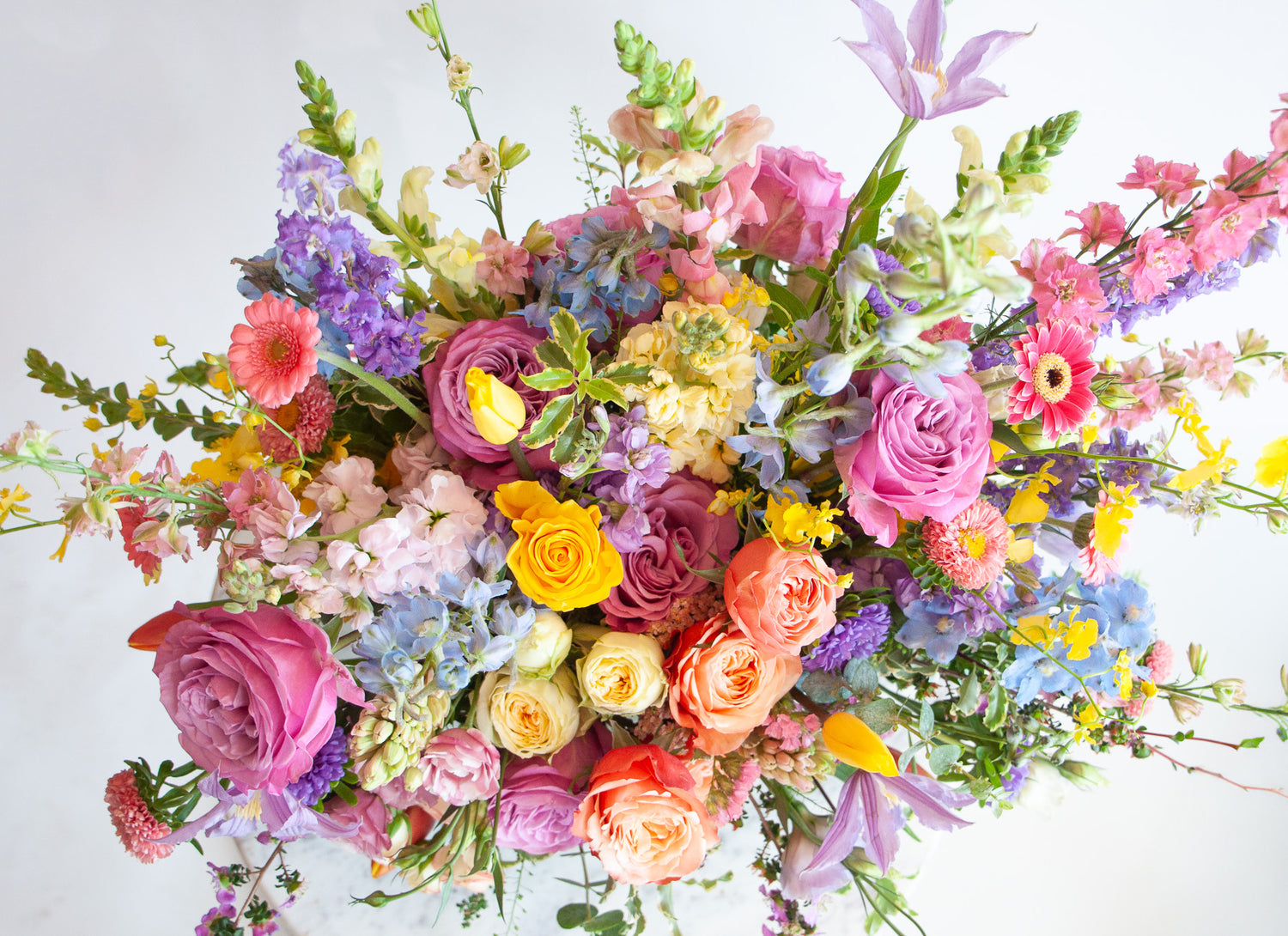 Close up of the blooms in a flower arrangement. The flowers are many colors and include roses, tulips, daisies, snapdragon, clematis, stock, hyacinth, orchids, and delphinium.