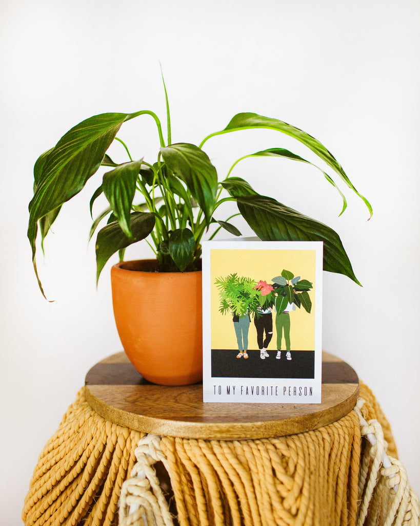 A greeting card that reads "to my favorite person". The artwork on it is of three people holding potted plants in front of their faces.