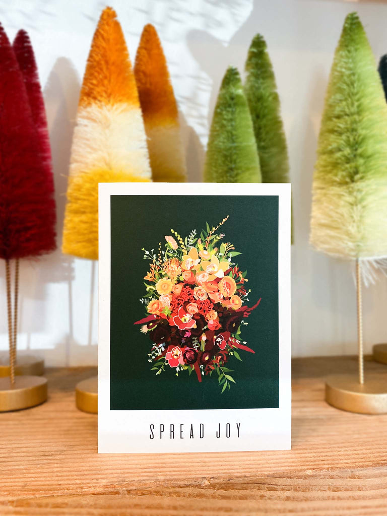 A greeting card that reads "spread joy". The artwork on it is of a gold and red flower bouquet on a dark green background.
