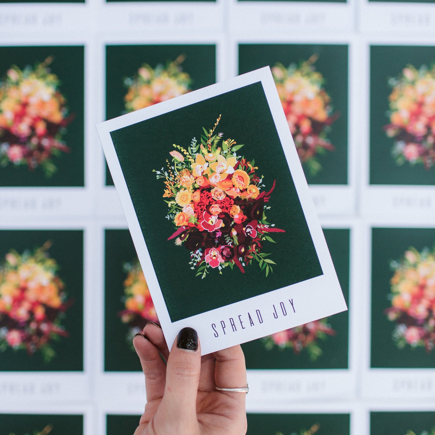 A greeting card that reads "spread joy". The artwork on it is of a gold and red flower bouquet on a dark green background.