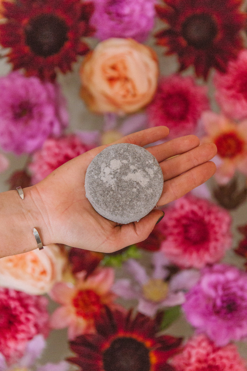 Hand holding a WildFlora Bath Soak in front of a colorful floral bath