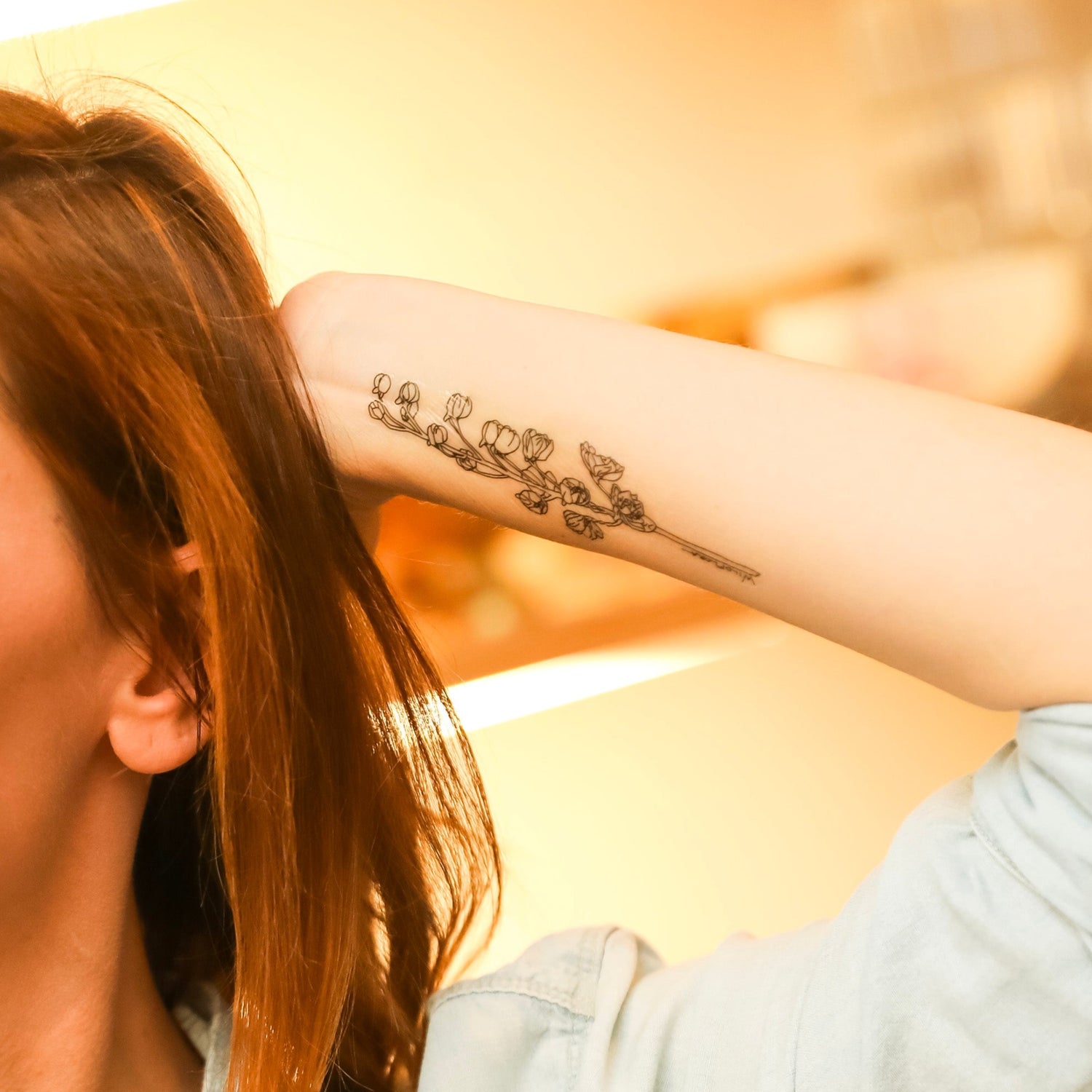 a closeup of a woman's forearm, adorned by a temporary delphinium line drawing tattoo.