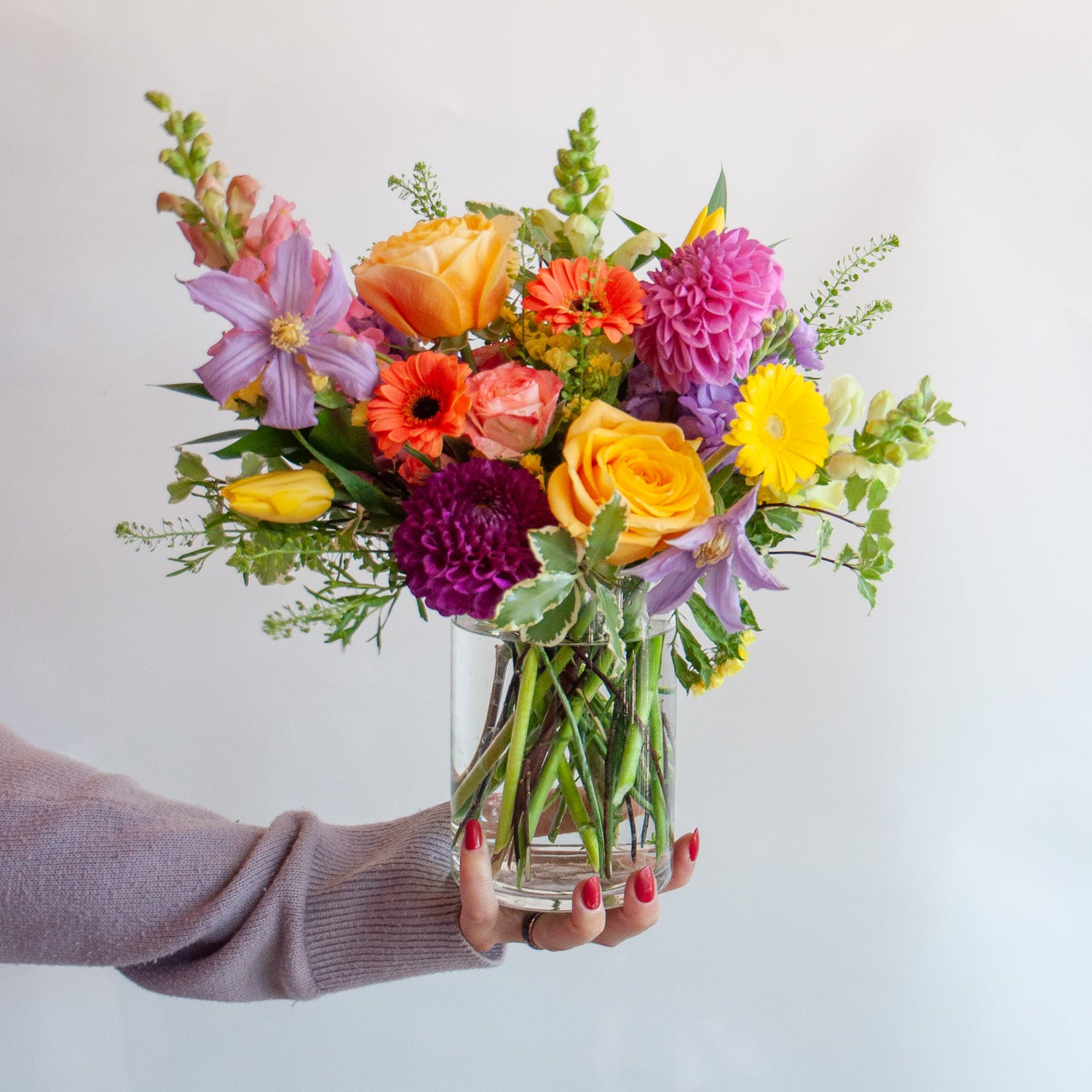 A hand holds a small hobnail arrangement with multi-colored blooms.
