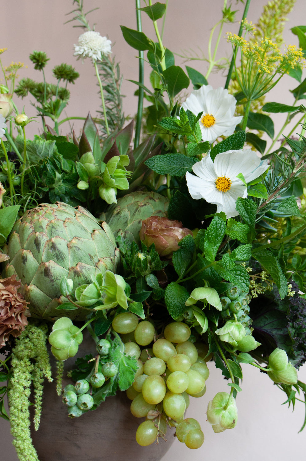 Arrangement of greenery, flowers, and fruits on a wooden surface with a neutral background