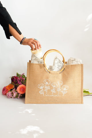 Person adding a candle to a jute WildFlora bag with flowers on a white background