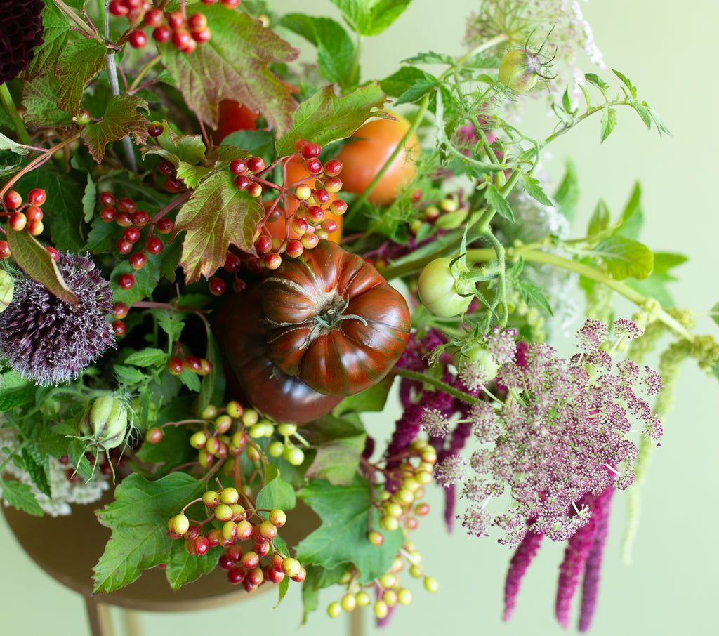 Decorative arrangement with fruits, vegetables, and flowers on a light green background
