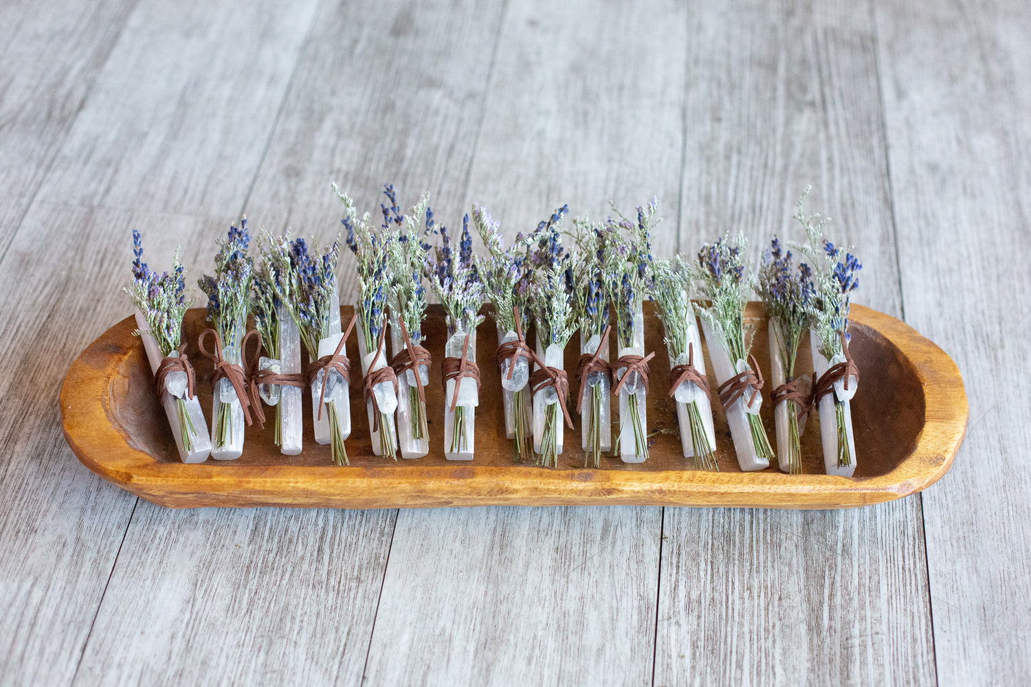 Bouquets of dried flowers tied to selenite crystals in a wooden tray.