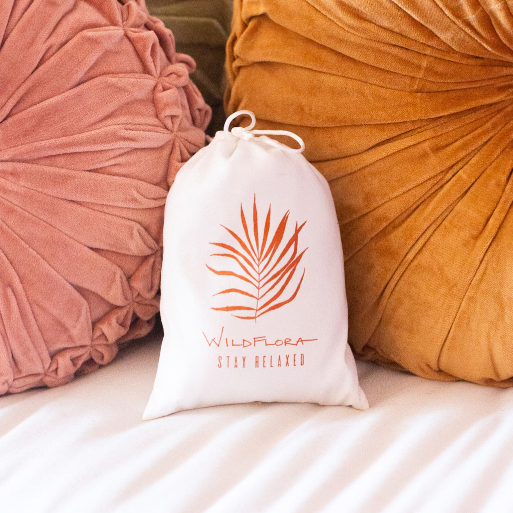 White drawstring bag with a palm leaf design on a bed with textured pillows.