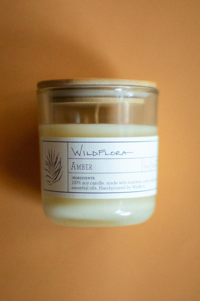 WildFlora Amber Candle in a glass jar with a label on an orange background