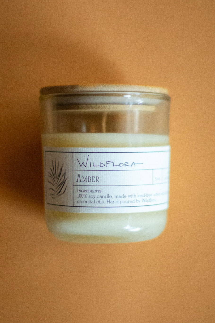 WildFlora Amber Candle in a glass jar with a label on an orange background