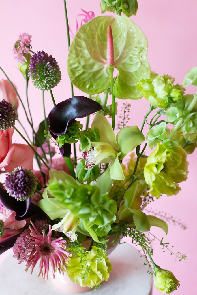 Pink & Green floral arrangement in a pink vase on a white pedestal against a pink background - very Glinda-Elphaba vibes