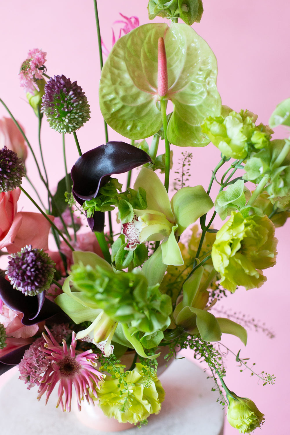 Pink & Green floral arrangement in a pink vase on a white pedestal against a pink background - very Glinda-Elphaba vibes