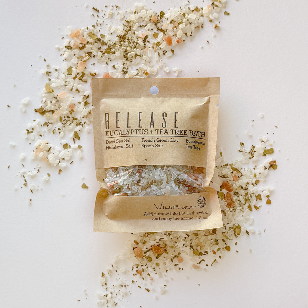 WildFlora Release Bath Salt Packet on a white background with flourishes of the salt laid around it.