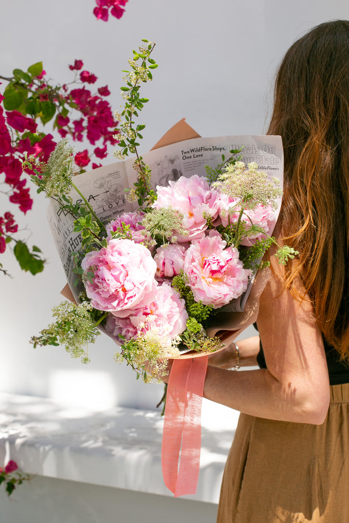 woman holding bouquet of pink peonies and white Queen Ann's Lace wrapped in paper