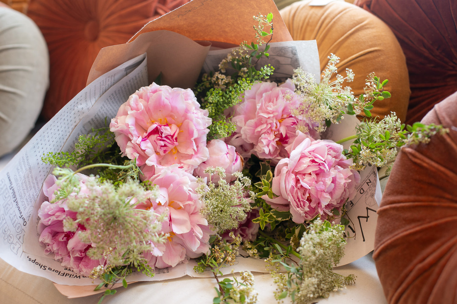 pink peonies and white Queen Ann's Lace bouquet in wrapped paper on a couch with pillows
