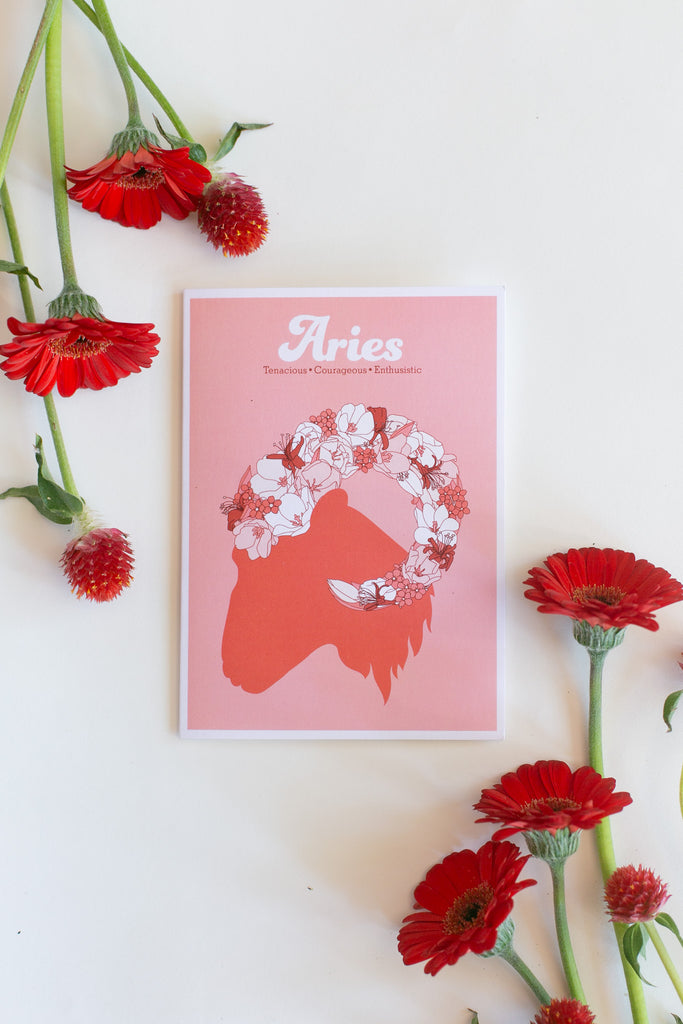 An Aries zodiac greeting card featuring a ram silhouette with a white floral crown, styled on a white background with red flowers.