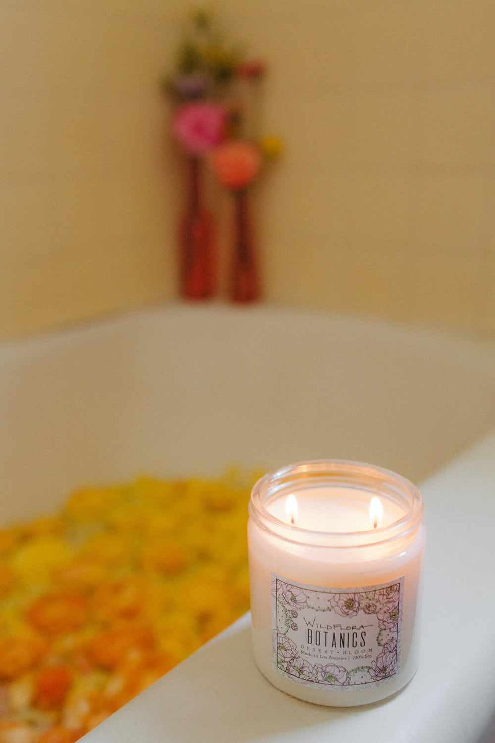 WildFlora double wick Botanics candle on a bathtub filled with water and flowers