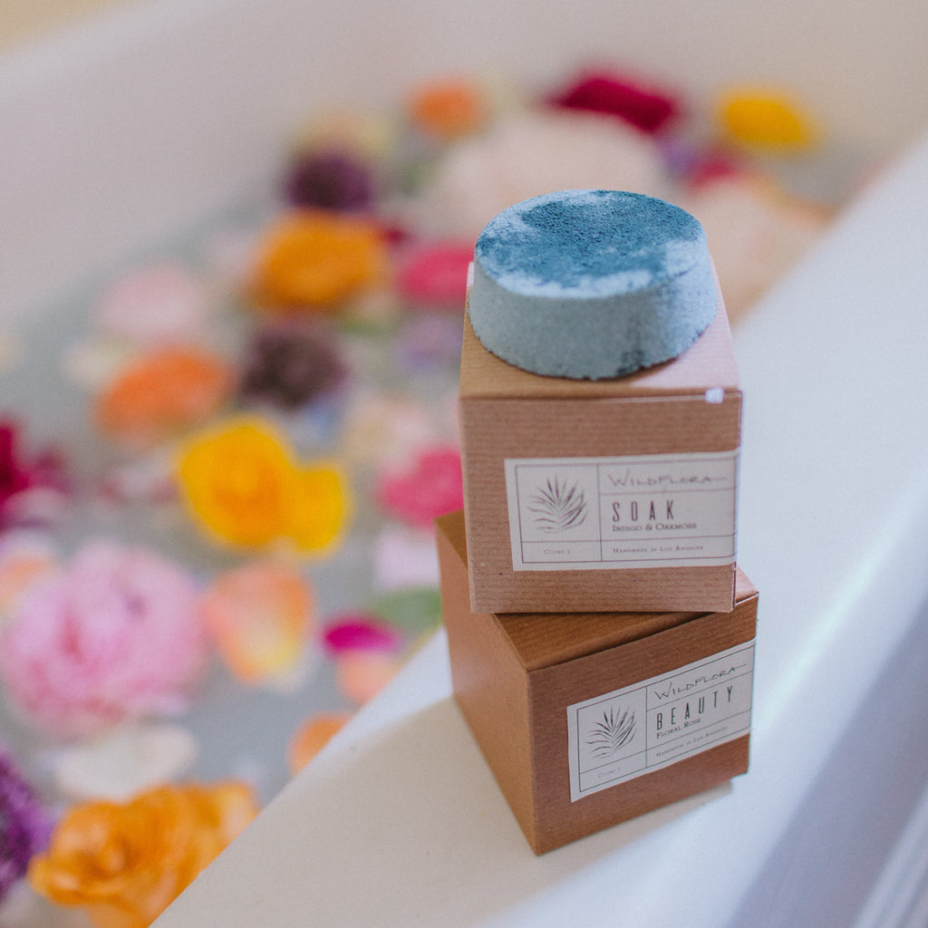 WildFlora Bath Soak with packaging on a bathtub rim with colorful flowers in the background