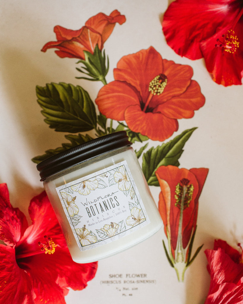 White WildFlora Hibiscus candle with a black lid on a hibiscus art background