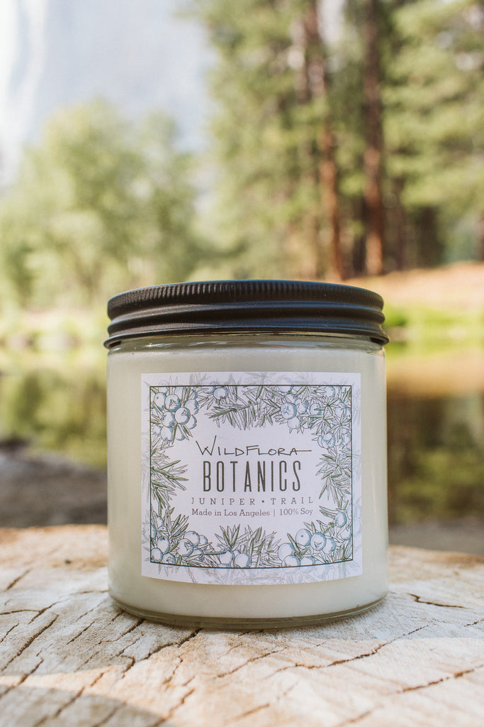 WildFlora double wick Botanics candle with a label on a wooden surface with a forest background