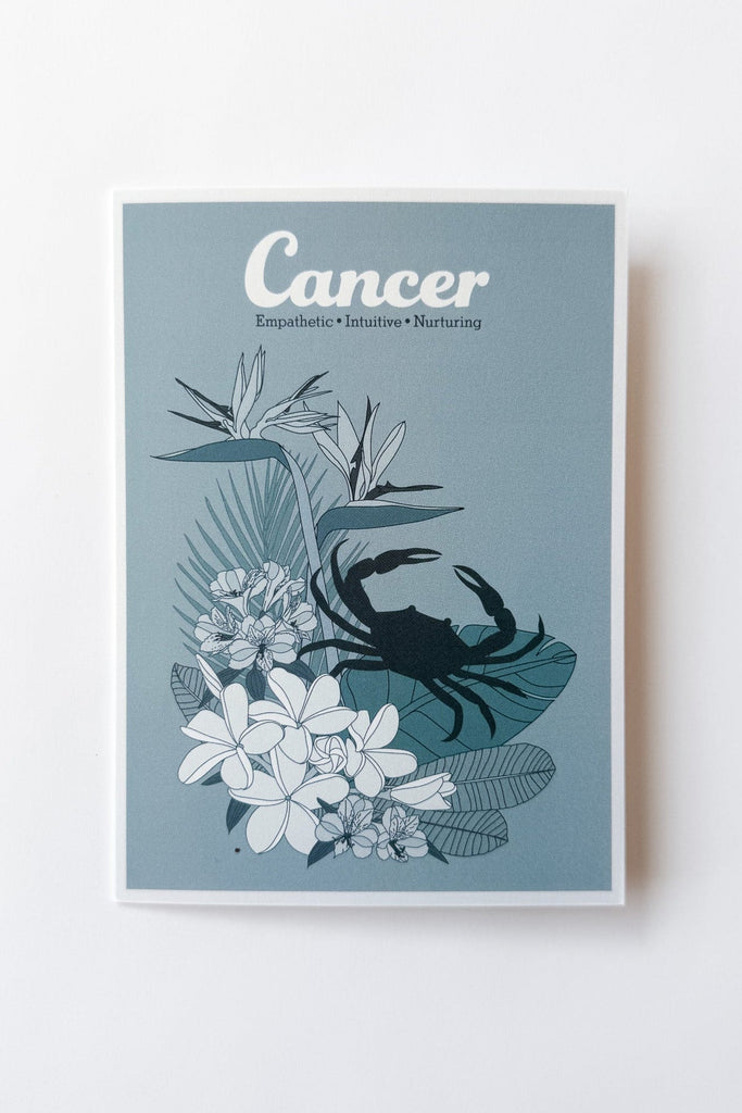 A vertical greeting card featuring a Cancer zodiac design with a blue crab silhouette over white tropical flowers and leaves on a muted blue background, shown against a plain white background.