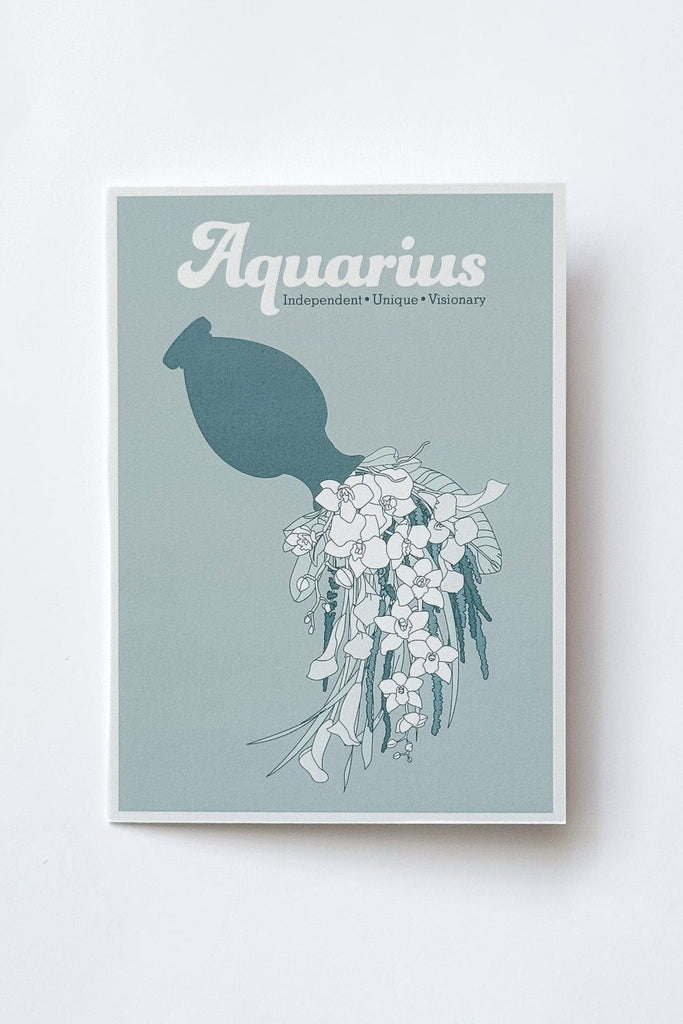 A greeting card featuring the word 'Aquarius' in white script above a teal silhouette of a jug pouring illustrated florals on a muted blue-green background, photographed against a white background.