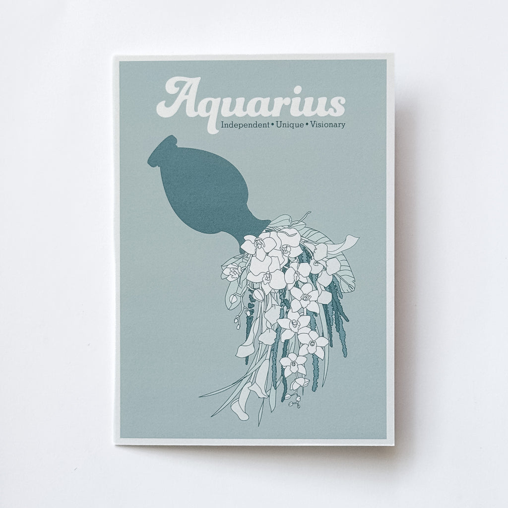 A greeting card featuring the word 'Aquarius' in white script above a teal silhouette of a jug pouring illustrated florals on a muted blue-green background, photographed against a white background.