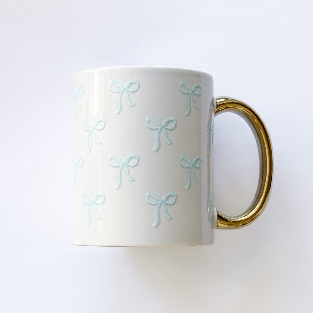 White mug with blue bow patterns and a gold handle on a white background