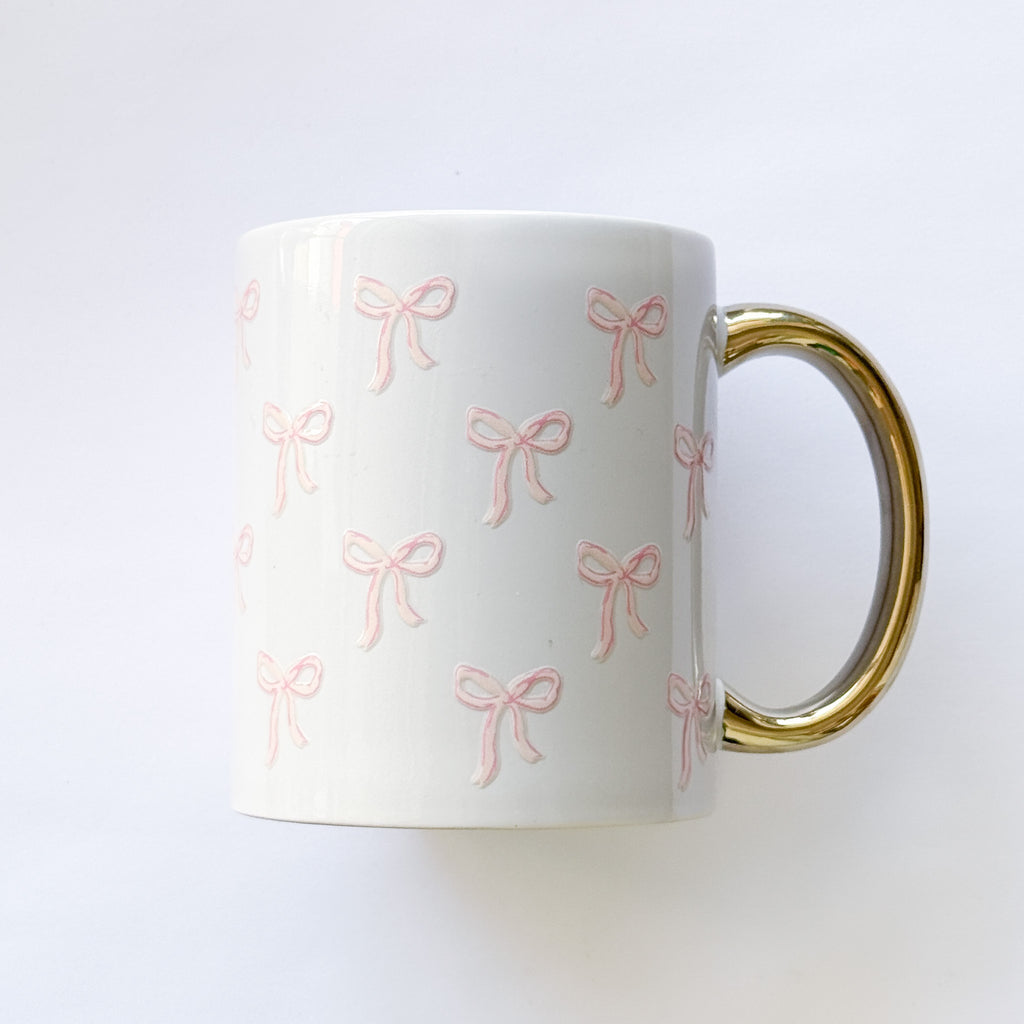 White mug with pink bow pattern and gold handle on a white background