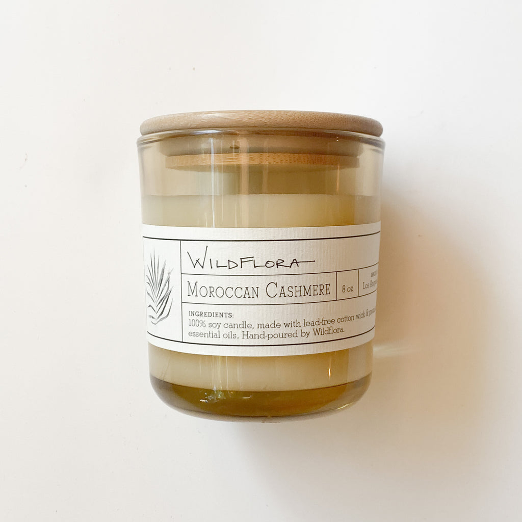 Moroccan Cashmere single-wick, white soy wax candle in a tan glass container with a wood lid. The label is apothecary style and shows the scent.
