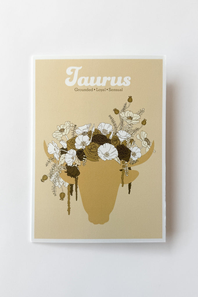 A greeting card featuring a beige background with the word 'Taurus' at the top and an illustrated silhouette of a bull's head filled with white and dark brown flowers. The print is photographed against a white background.