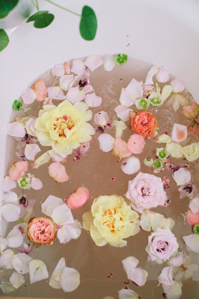 Floral bath with pink, yellow, and white flowers floating in water on a white background