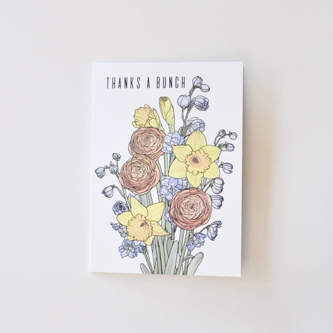 A greeting card that says "thanks a bunch" and has artwork of ranunculus, daffodils, and delphinium on it.