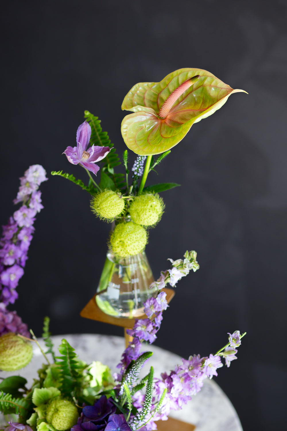 chartreuse and purple flowers in a glass beaker on a marble table against a dark background