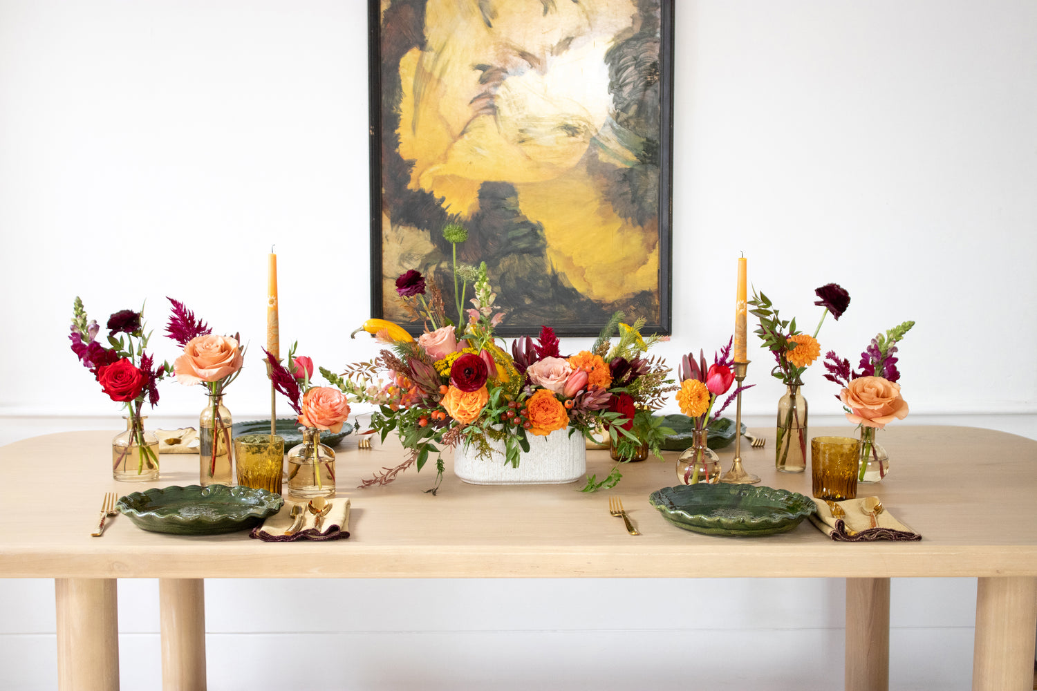 WildFlora's Gathered Garden Arrangement and Bud Vases in a ribbed long and low white speckled container on a Thanksgiving table. It includes orange, tangerine, red, pink, fuchsia, maroon, and gold flowers, complete with festive gourds / mini pumpkin, ranunculus, rose, dahlia, yarrow, weeping amaranthus, chocolate cosmos, delphinium, lisianthus, tulip, Queen Anne's lace, evergreens, snapdragon, and hypericum berries.