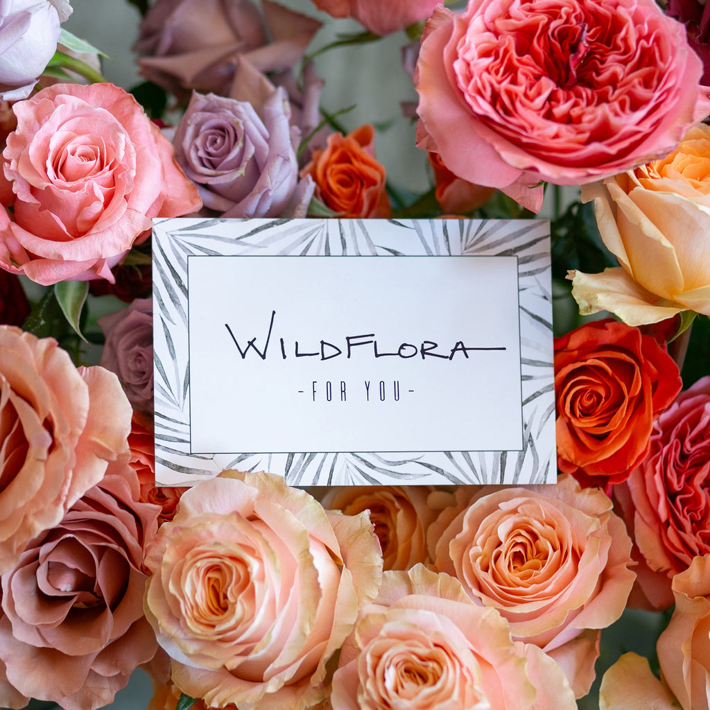 a WildFlora gift card sits amonst pink, purple, peach, tan, and orange roses.