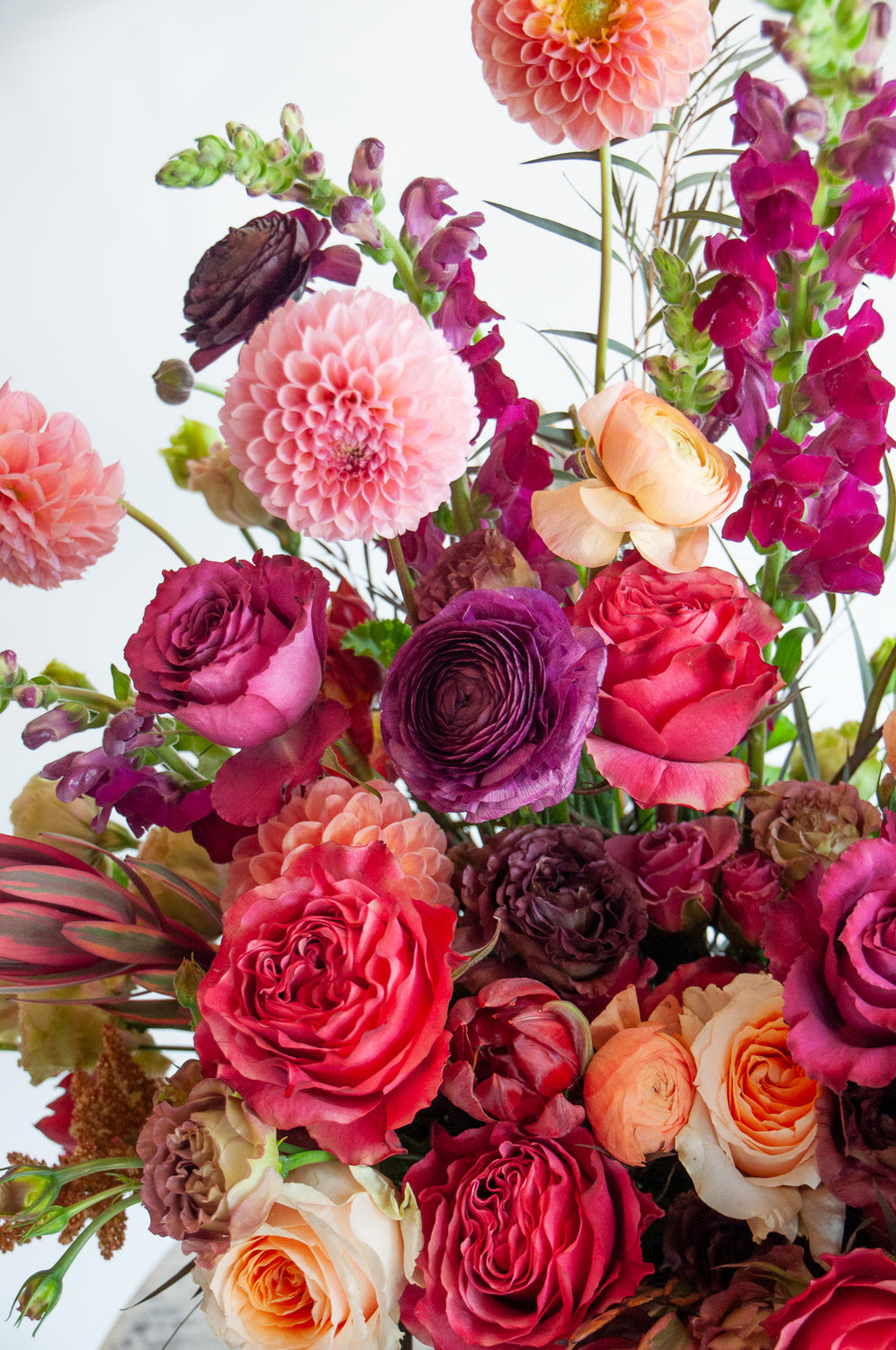 closeup of A red, peach, pink, and eggplant WildFlora flower arrangement in a spherical terracotta vase, featuring rose, ranunculus, dahlia, lisianthus, amaranthus, and snapdragon.