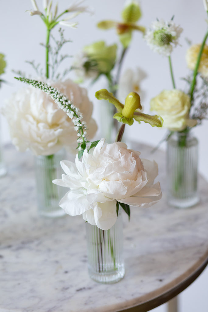 WildFlora's Snowy Days Bud Vases on a small marble table in front of a white backdrop. They have green, white, and chartreuse flowers, and include rose, veronica, scabiosa, pitcher flower, lily, and peony.