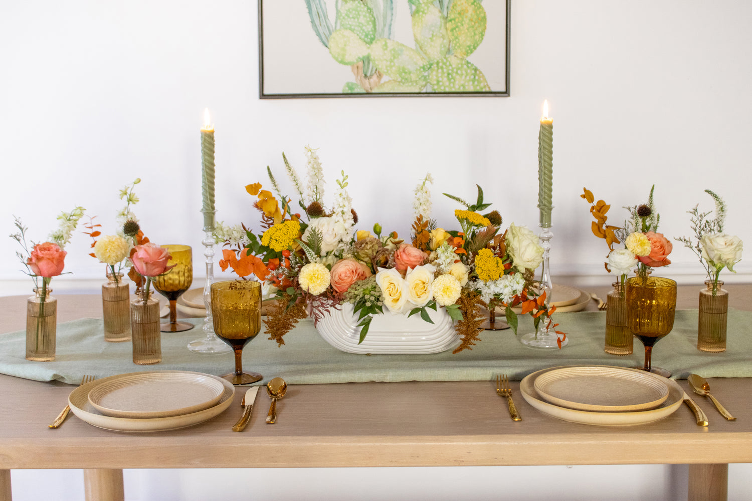 WildFlora's Gathered Garden Arrangement in an art deco white long & low container & Bud Vases in tan ribbed glass vases a on Thanksgiving table. They include coral, yellow, gold, brown, orange, and white flowers and foliage, complete with roses, spray roses, weeping amaranthus, delphinium, lisianthus, echinacea, yarrow, ranunculus, and marigold. 