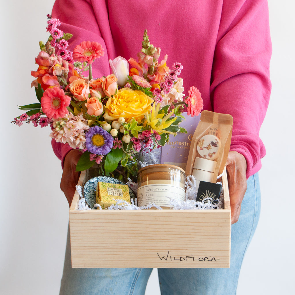 woman holding a wildflora classic gift box with candle flowers chocolate soap dish shower steamers and matches