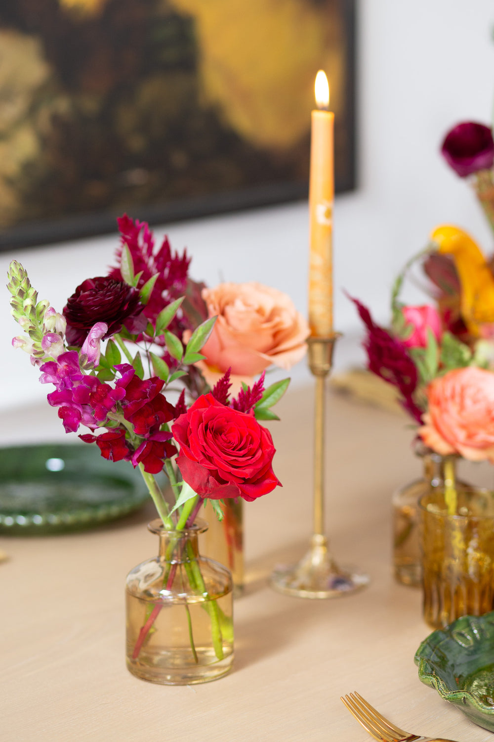 WildFlora's Gathered Garden Bud Vases in tan glass vessels on a Thanksgiving table. They include orange, tangerine, red, pink, fuchsia, maroon, and gold flowers, complete with ranunculus, rose, dahlia, celosia, lisianthus, tulip, and snapdragon.