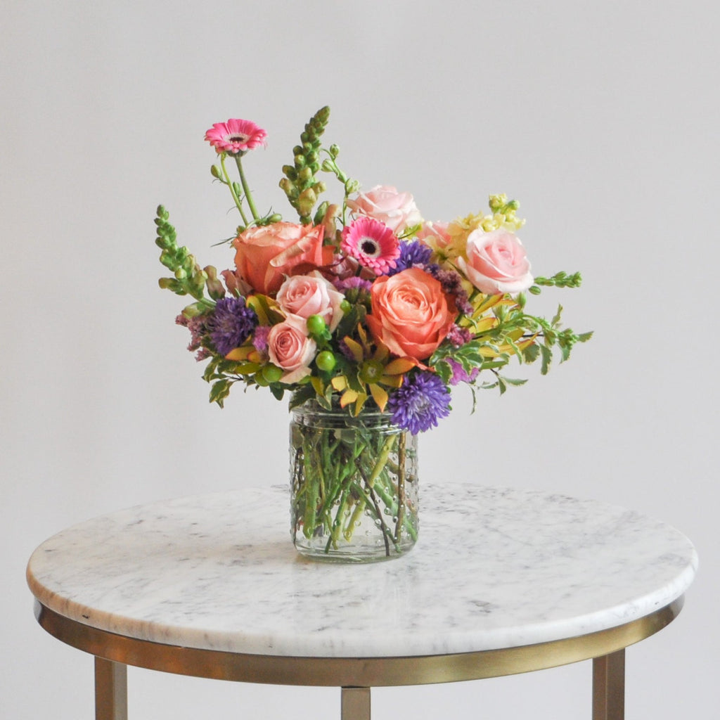 A small hobnail arrangement sits on a marble table with multi-colored blooms.